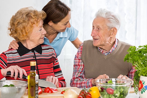 An elderly couple eating together with the help from a live-in carer.