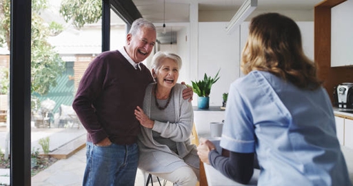 An elderly couple laughing at home with a private nurse