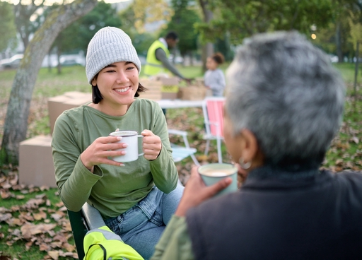 A live-in carere and and elderly man having a hot drink sitting outside.